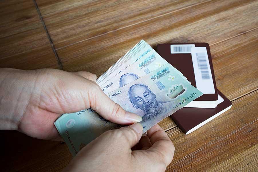Woman hand hold for counting Vietnam Dong banknote with passport book on wood table